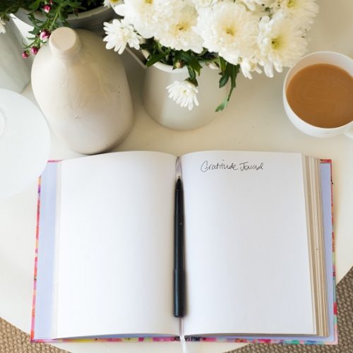 blank gratitude journal with pen on desk with tea and flowers