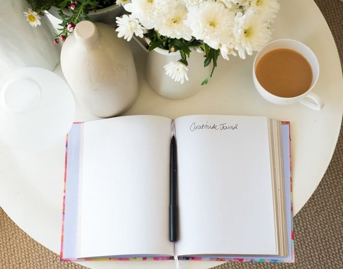 blank gratitude journal with pen on desk with tea and flowers