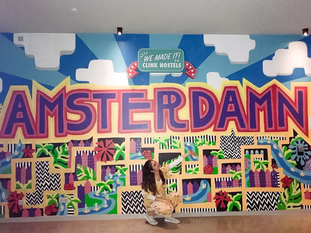 monica nedeff the traveling dietitian posing by a mural at Clink Hostel in Amsterdam
