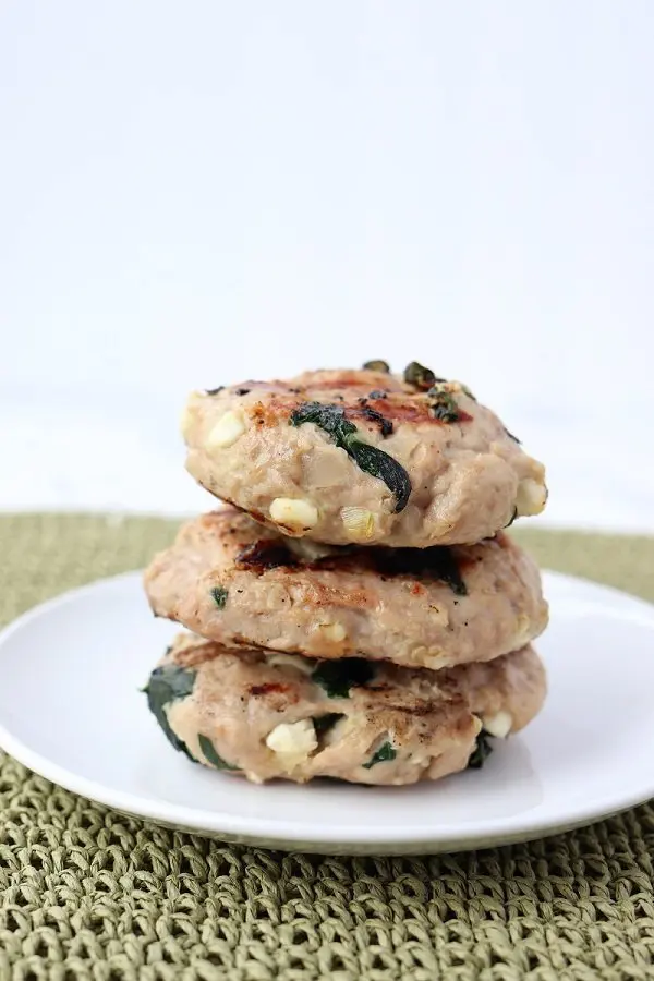 three grilled turkey burgers with chunks of feta and spinach stacked on a plate