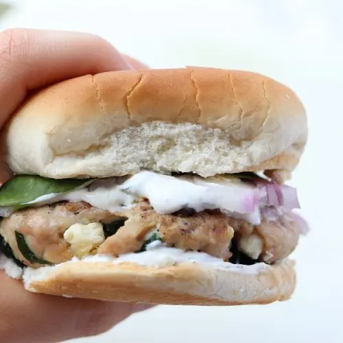 Hand holding a turkey burger with tzatziki dripping down the bun