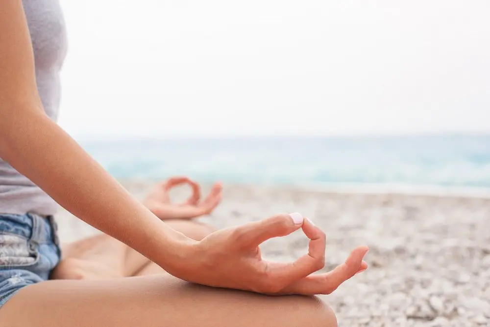 girl meditating on the beach with hands resting on legs