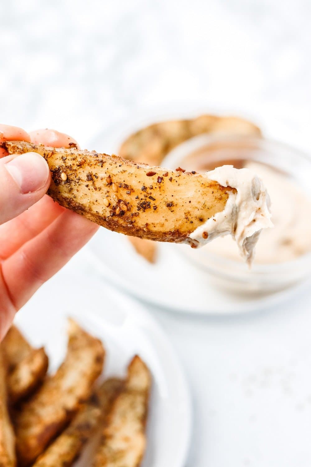 close up of a handheld fry dunked in tahini sauce