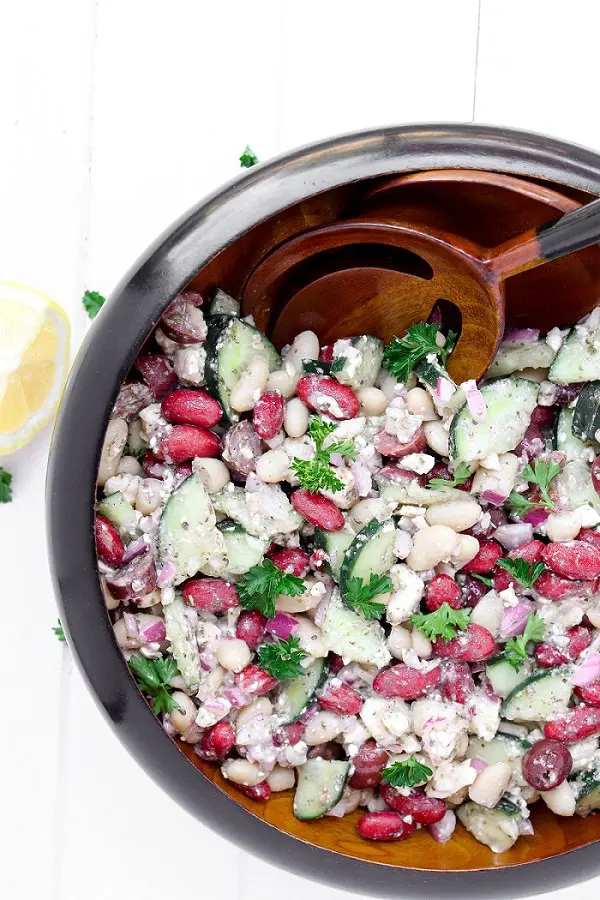 Large wooden serving bowl of bean salad with a wooden spoon