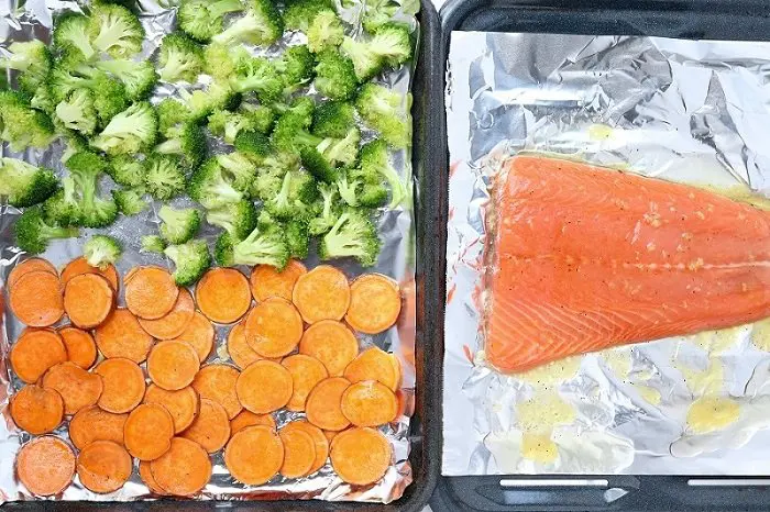salmon and vegetables on separate foil lined sheet pans ready for broiling