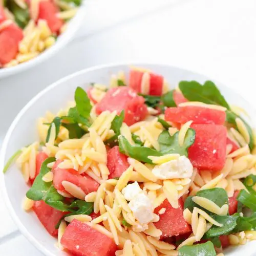 white bowl of orzo mixed with watermelon, feta cheese and arugula