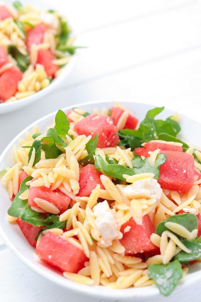 close up of chopped watermelon, orzo and arugula in a salad bowl