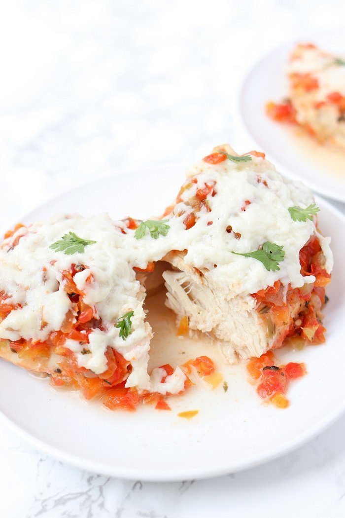 chicken breast topped with cheese and cilantro cut in half on a white plate