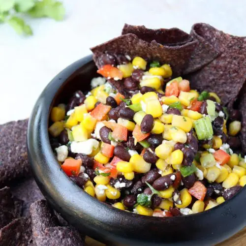 black tortilla chips sitting in a bowl of black bean and corn salad