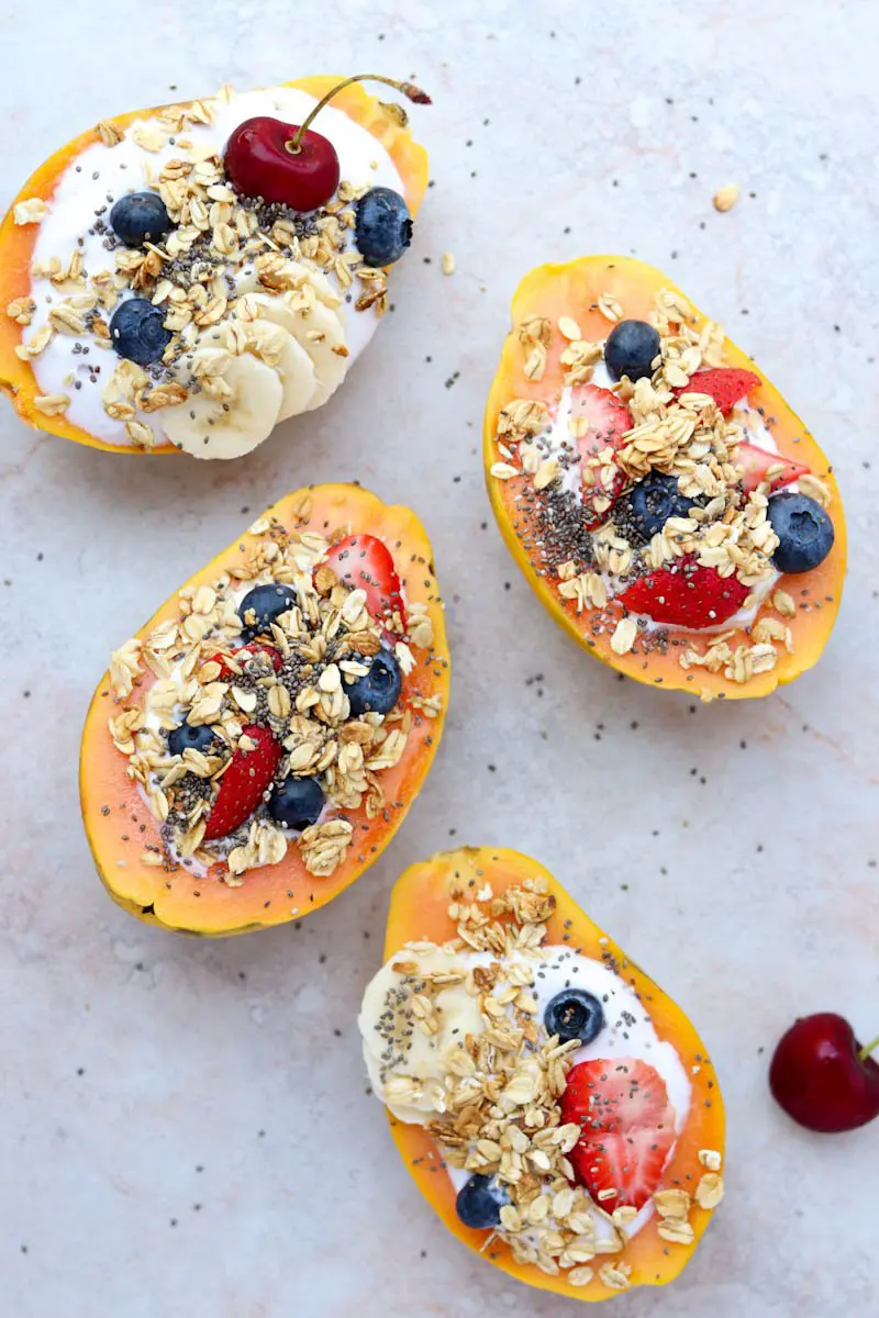 four papaya halves facing upward filled with fruit and granola