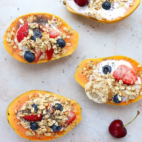 papayas sliced in half facing upwards and topped with yogurt and fruit