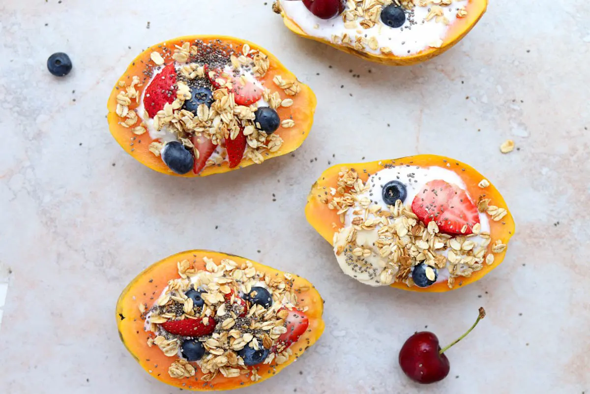 papayas sliced in half facing upwards and topped with yogurt and fruit