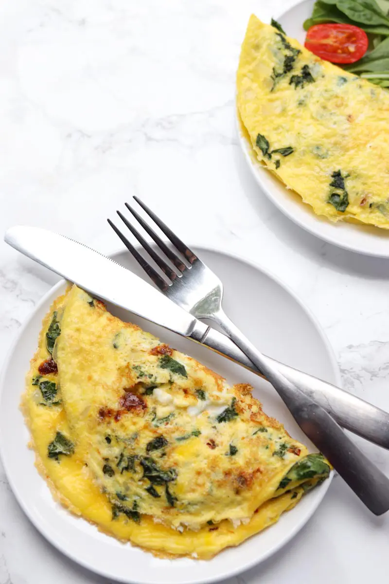 two omelettes on separate white plates with a fork and knife resting one plate