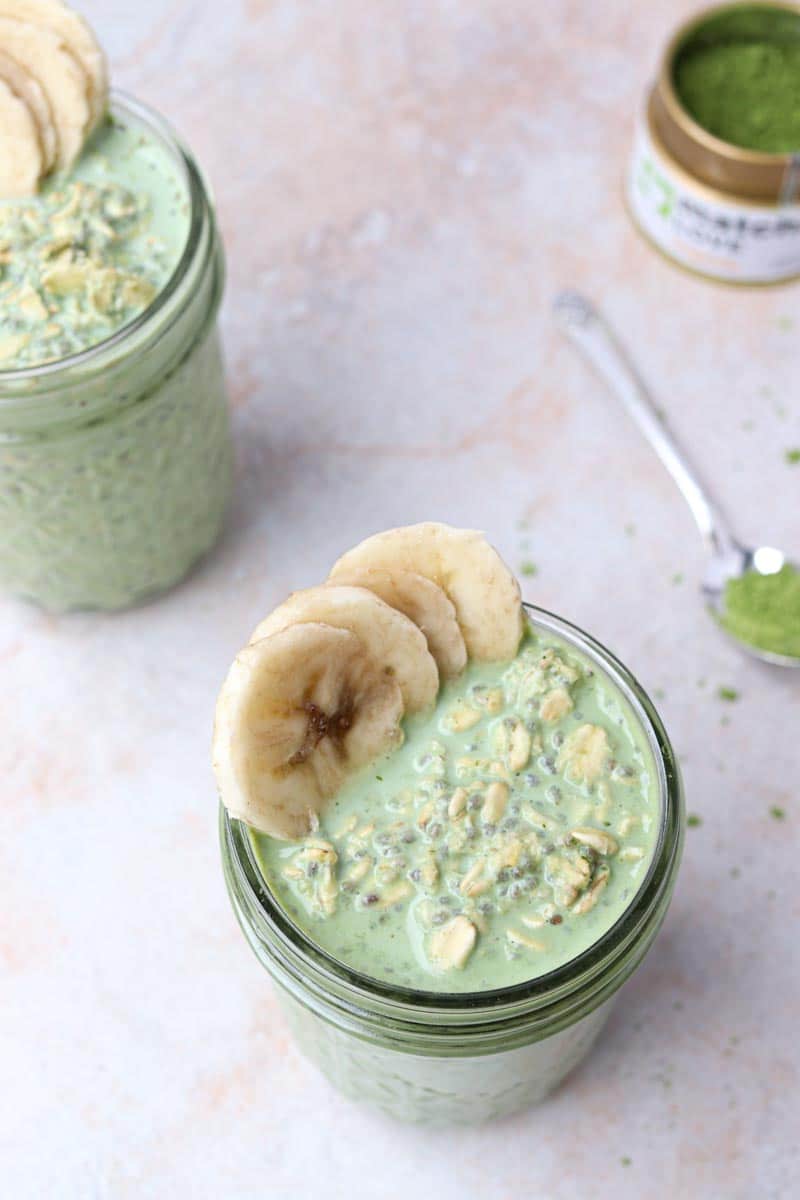 two jars of overnight oats with chia seeds, matcha powder and banana slices garnishing the glass