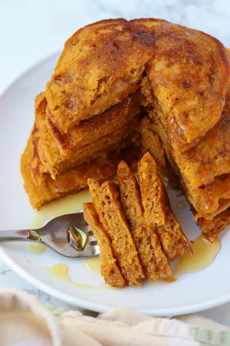 fork holding a bite of syrup covered pancakes next to a stack of sliced pancakes