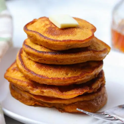 five pumpkin pancakes staked on a plate with a pad of butter on top