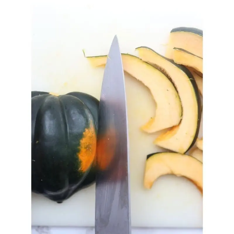 Knife slicing acorn squash into slices on a cutting board