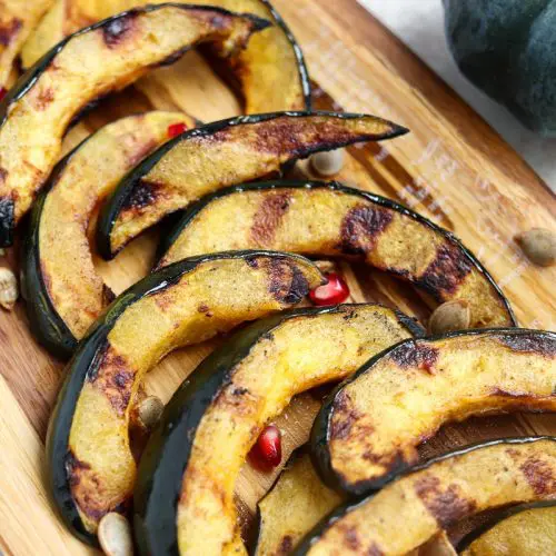 acorn squash slices with grill marks laying on a platter topped with roasted acorn seeds