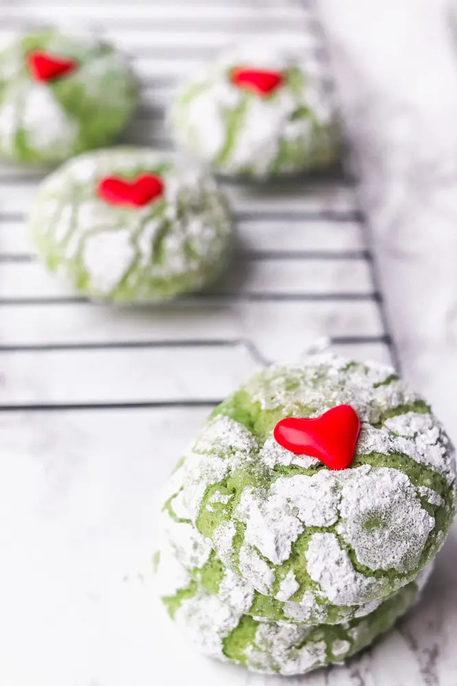 Green crinkle cookies stacked on top of each other with hearts on top.