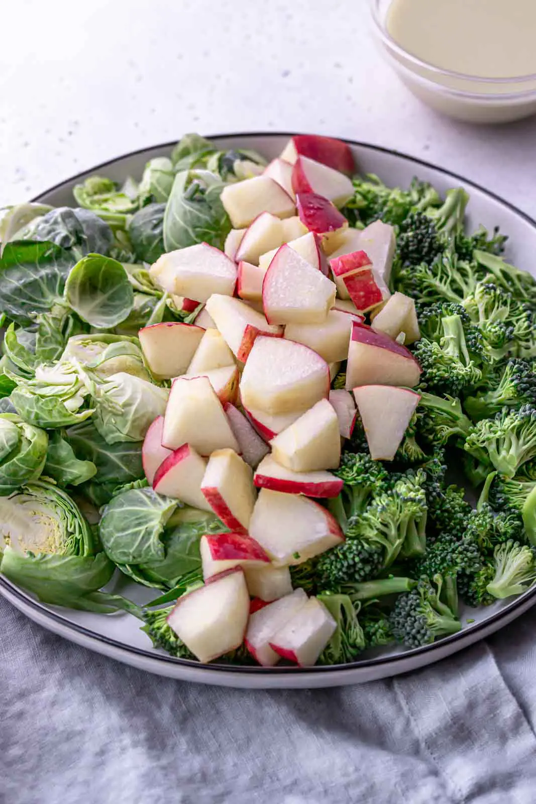 large plate of raw brussels sprouts, apples and broccoli