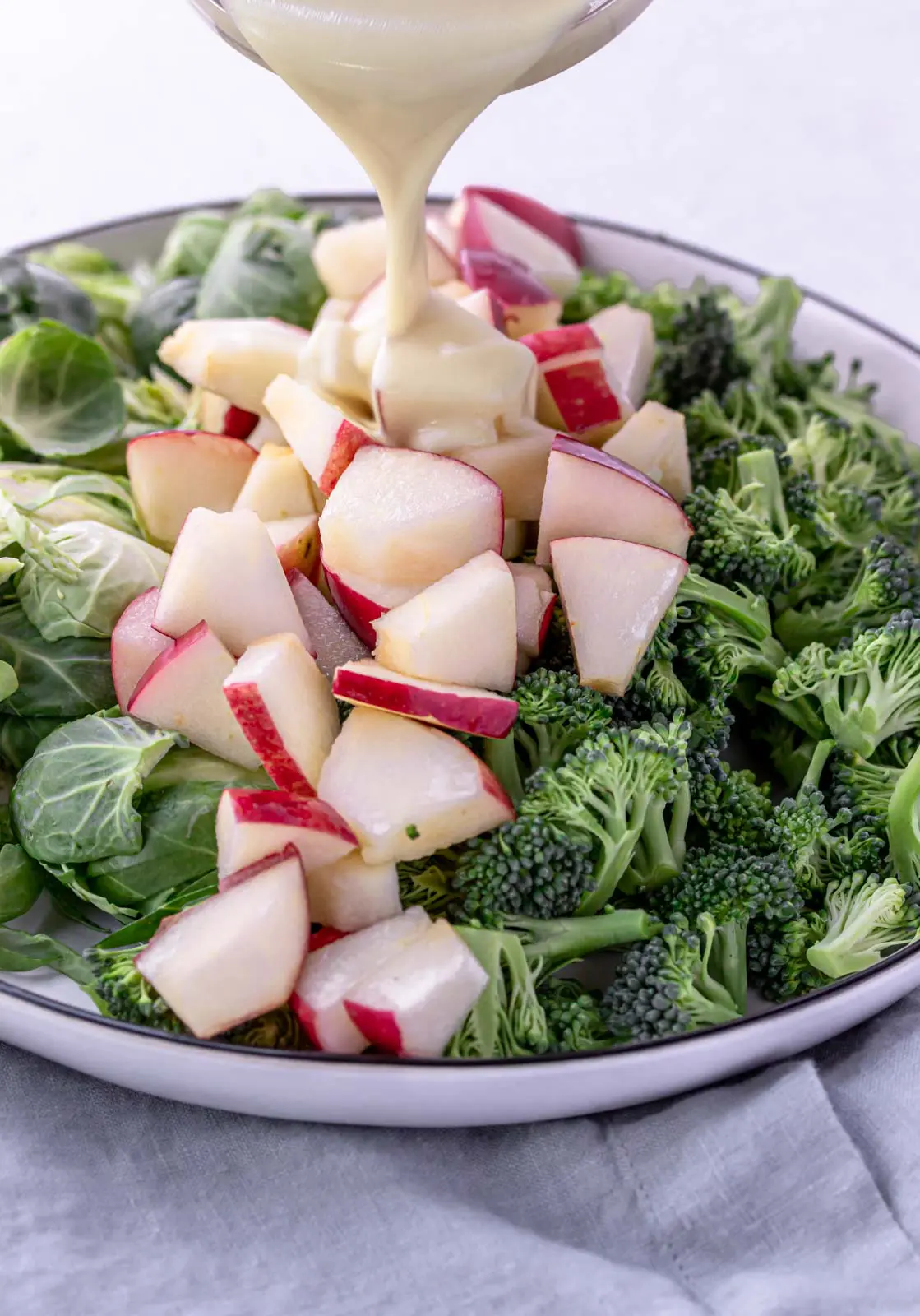 bowl pouring honey mustard dressing over apples and salad