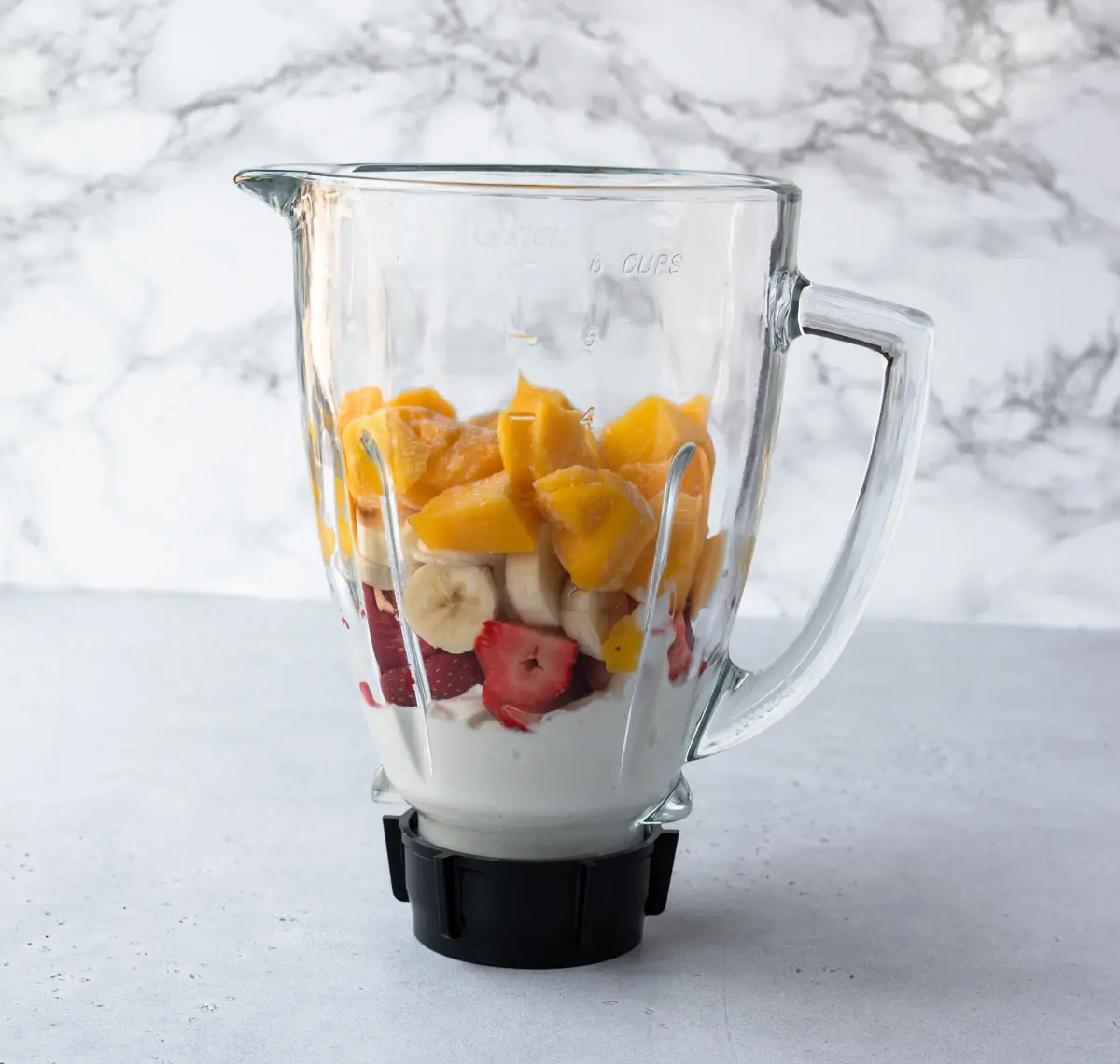 Blender holding Greek yogurt, fresh strawberries, banana and frozen mango