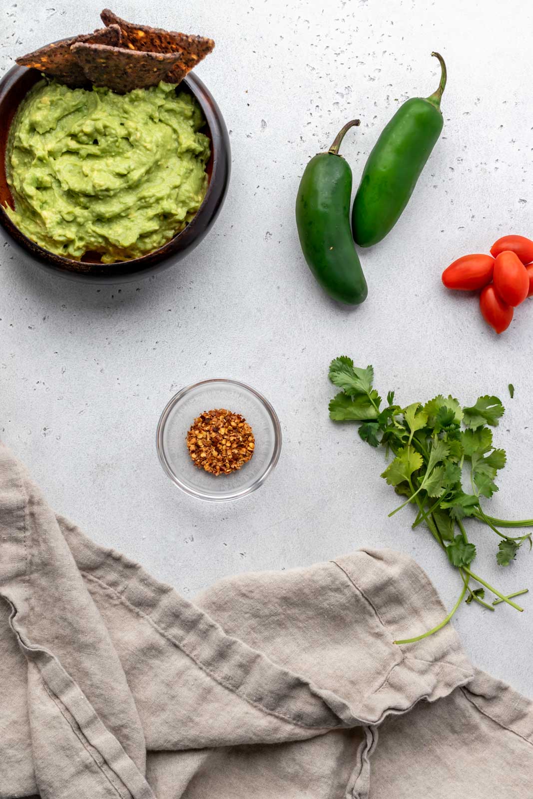 bowl of guacamole with jalapenos, cilantro and tomatoes laying next to it 