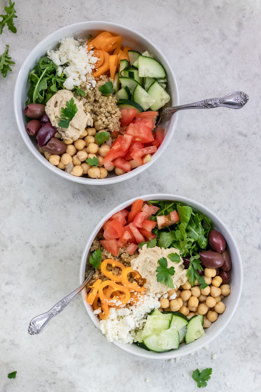 two bowls of quinoa, hummus, herbs and vegetables