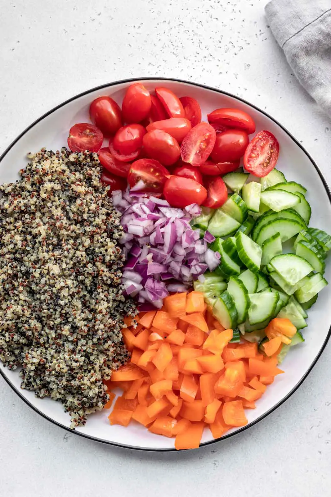 Platter of cooked quinoa, peppers, tomatoes and cucumber