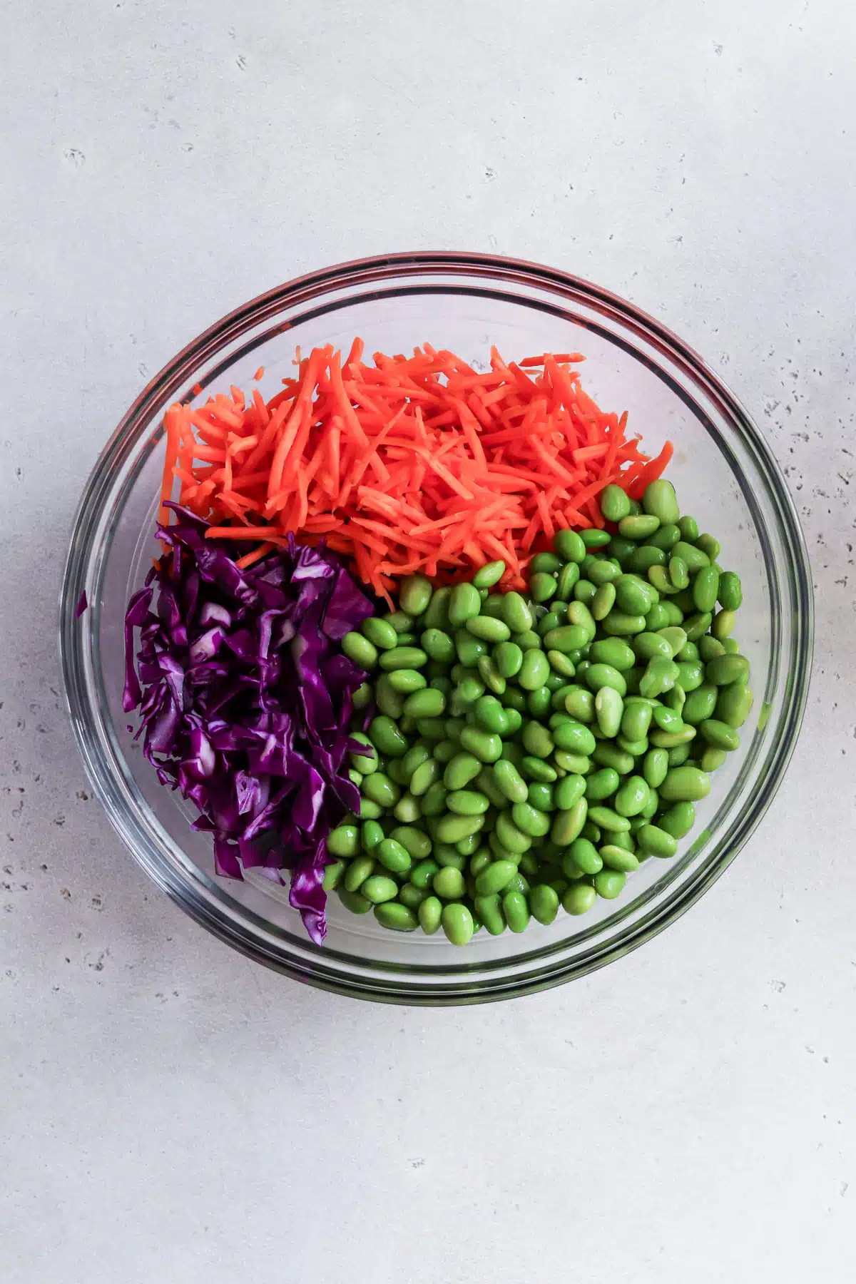 Mixing bowl of shredded carrots, chopped red cabbage, shelled edamame.